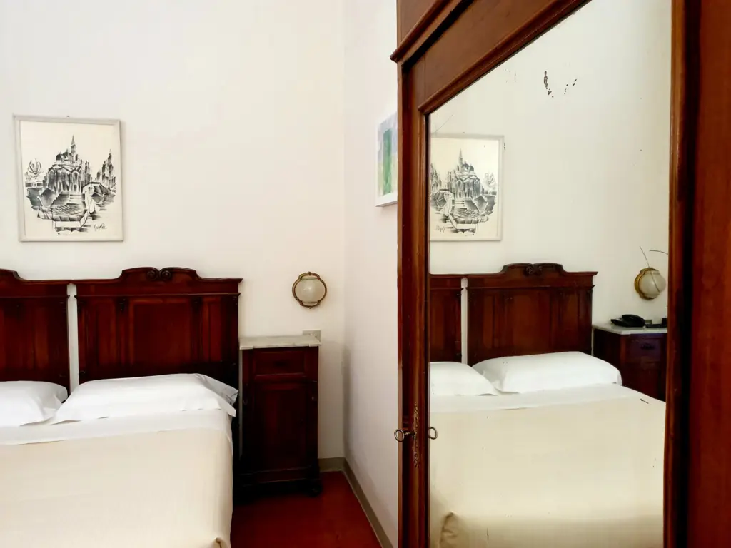 Double room with a carved wooden bed reflected in a mirror