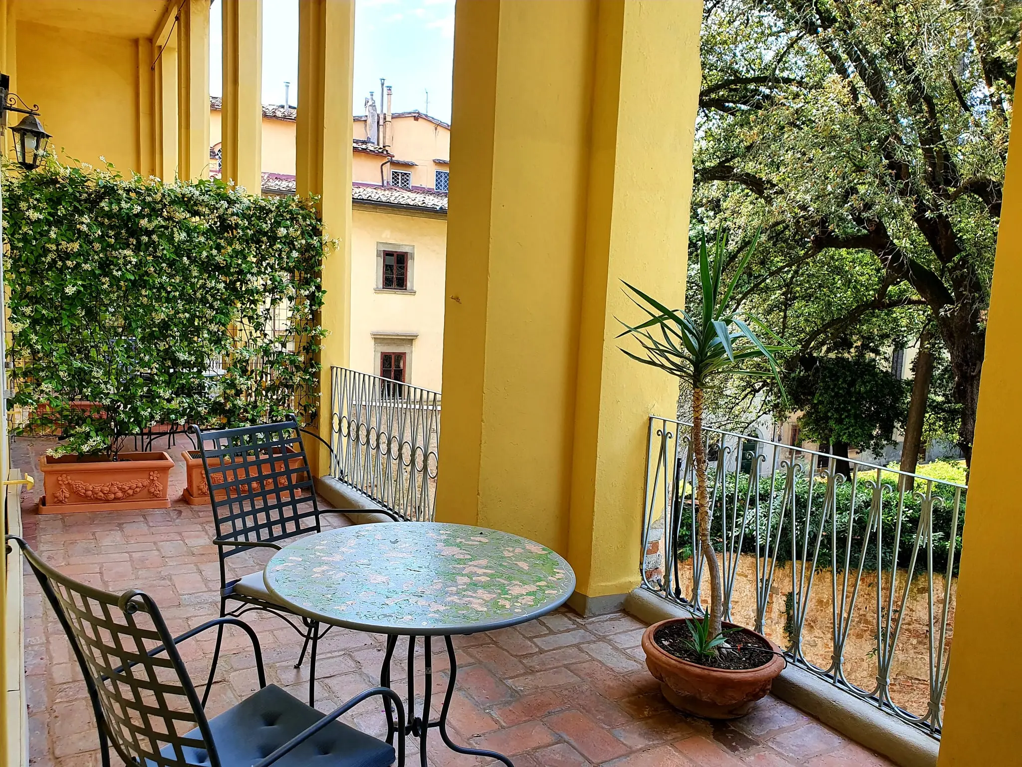 Loggia with yellow columns, a mosaic table and wrought-iron chairs above the garden
