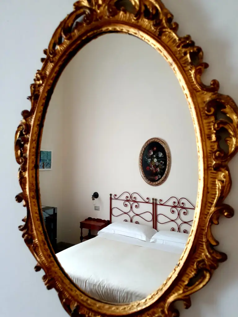 Carved gilded mirror reflecting a bedroom