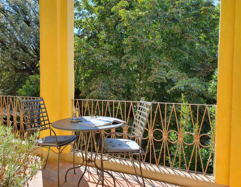 Balcony between yellow columns with a table and chairs in the greenery