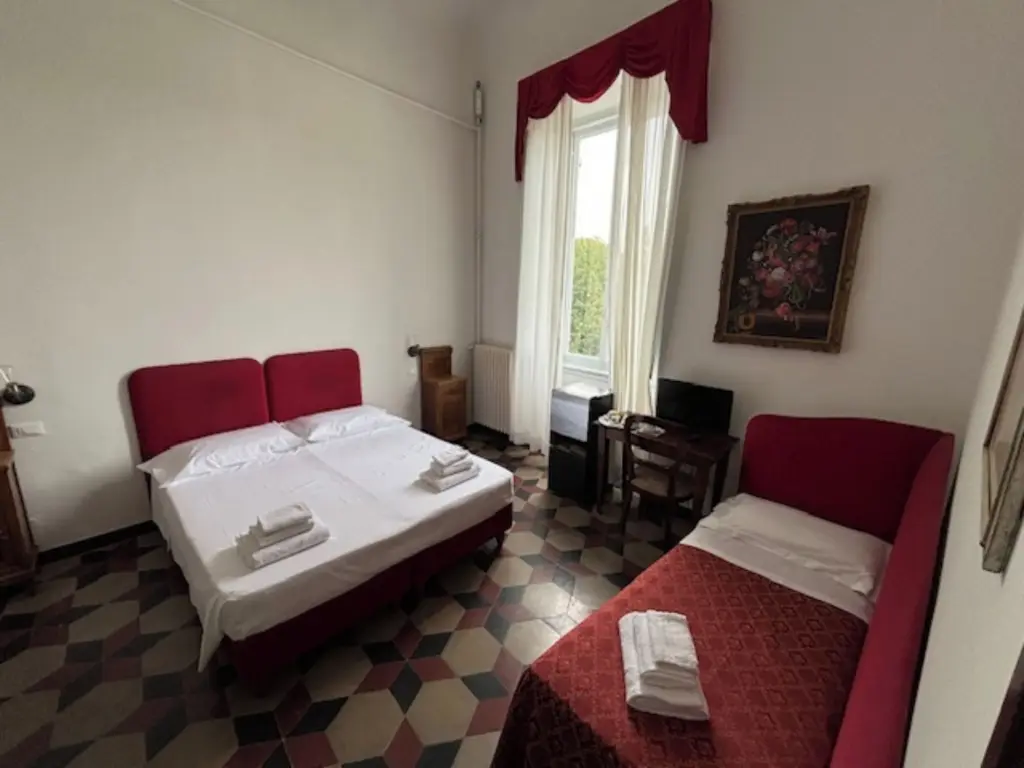 Camera tripla con letto matrimoniale e letto singolo in rosso, scrivania e alte finestre con tende