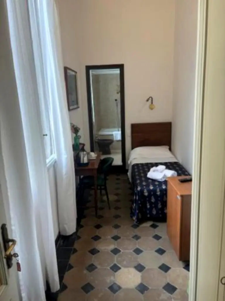 Camera singola con letto singolo, scrivania e porta del bagno socchiusa